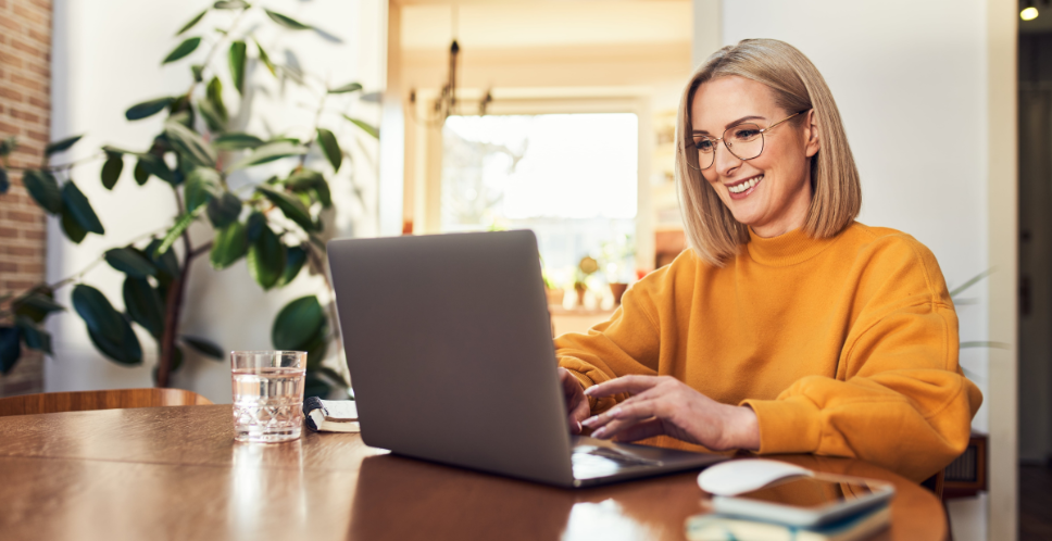 vrouw met gele trui en bril zit tevreden achter een laptop